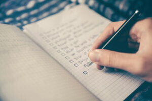 Hand schreibt eine Trainings-Checkliste in ein Notizbuch